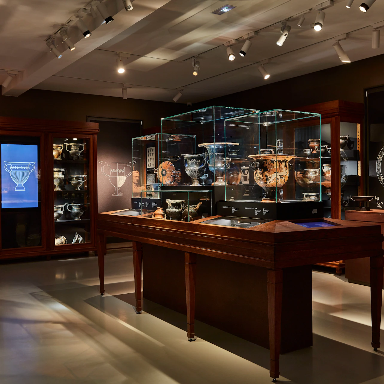 A museum exhibit featuring glass display cases with ancient pottery and artifacts, illuminated under spotlights in a dim room.