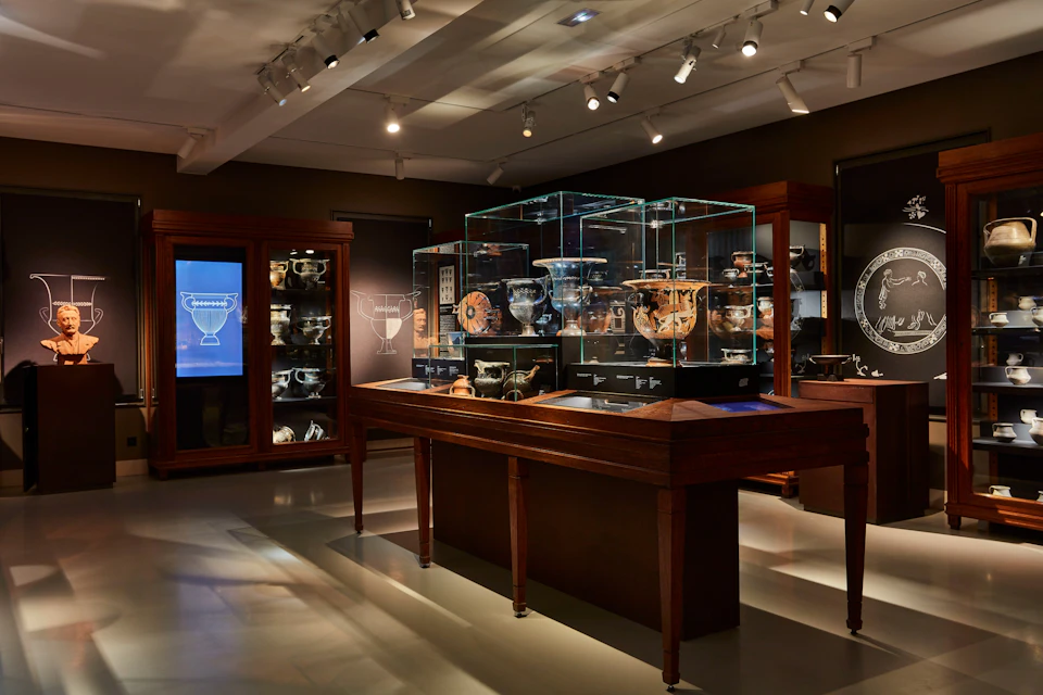 A museum exhibit featuring glass display cases with ancient pottery and artifacts, illuminated under spotlights in a dim room.