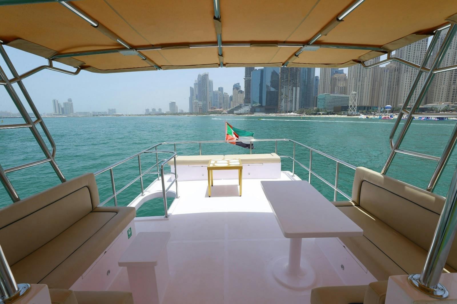 View from a yacht's deck overlooking the ocean and a city skyline, with seating, a table, and a flag visible.