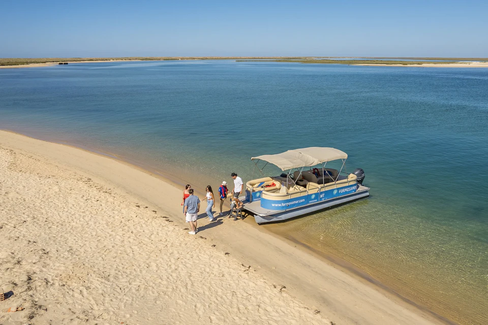 Guests disembarking from Formosamar boat onto Deserta Island´s sandy beach by calm blue water, under a clear sky.