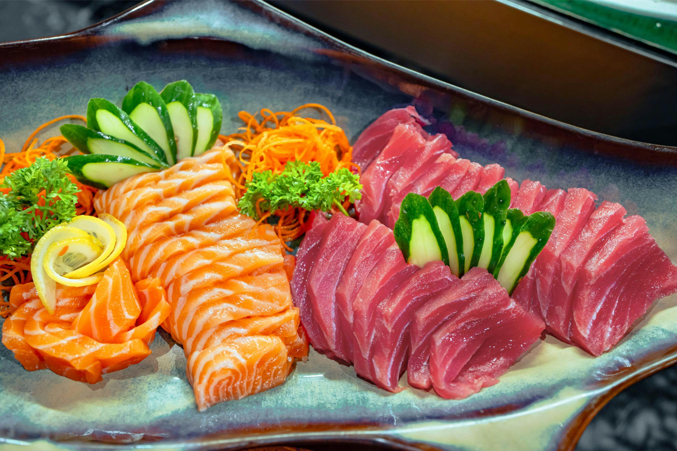 A plate of sashimi featuring sliced salmon and tuna garnished with cucumbers, shredded carrots, and parsley.