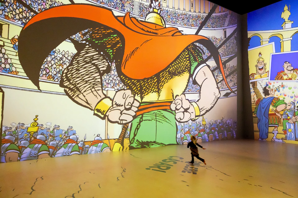 A child runs in front of a large projected comic-style image of a gladiator in an arena filled with spectators.
