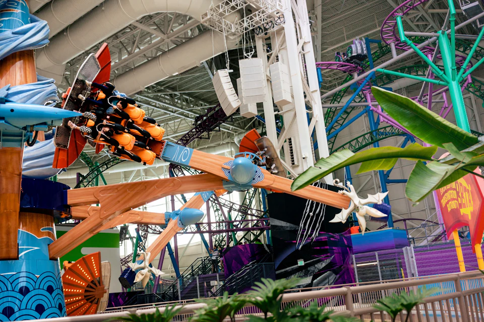 An indoor amusement park with a spinning ride and roller coaster tracks visible, surrounded by vibrant decorations.
