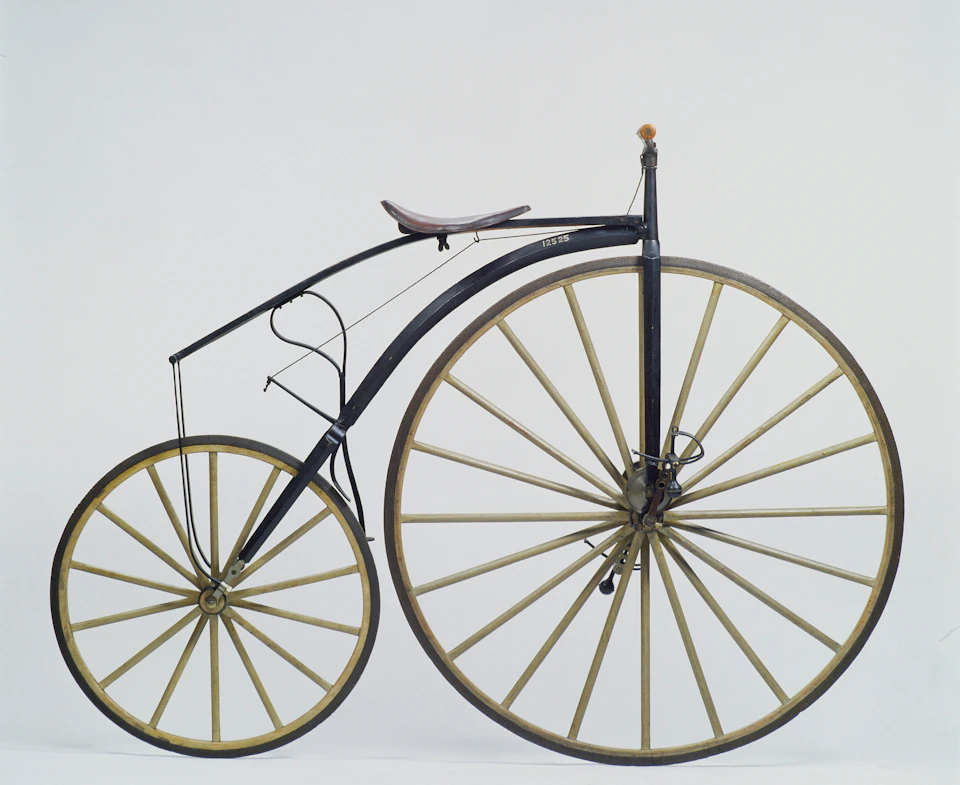 Antique bicycle with a large front wheel, smaller rear wheel, and a curved black metal frame against a plain white background.