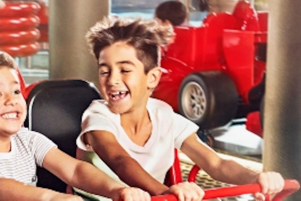 Children riding miniature red race cars on a track in an indoor amusement park.