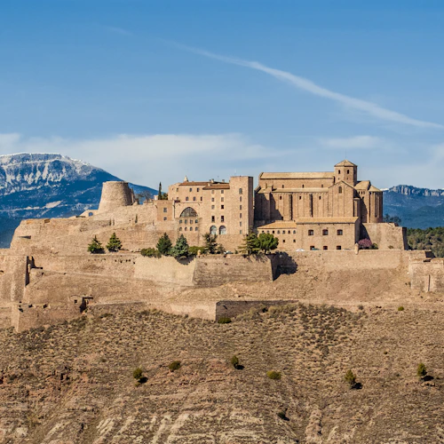 En stor stenborg på toppen av ett berg, med snötäckta toppar i bakgrunden och en blå himmel ovanför.