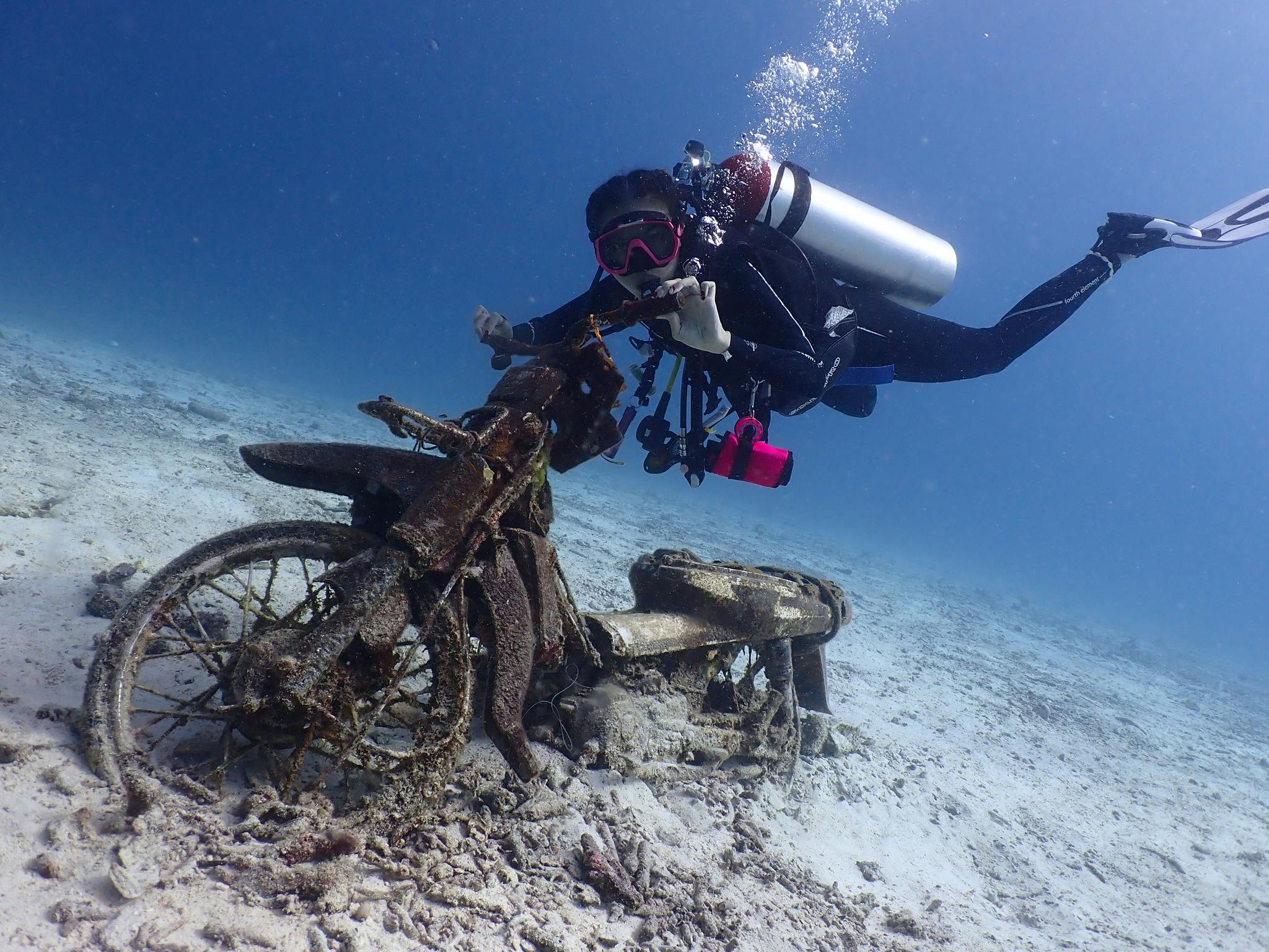 Podwodny płetwonurek badający zardzewiały motocykl na dnie oceanu.