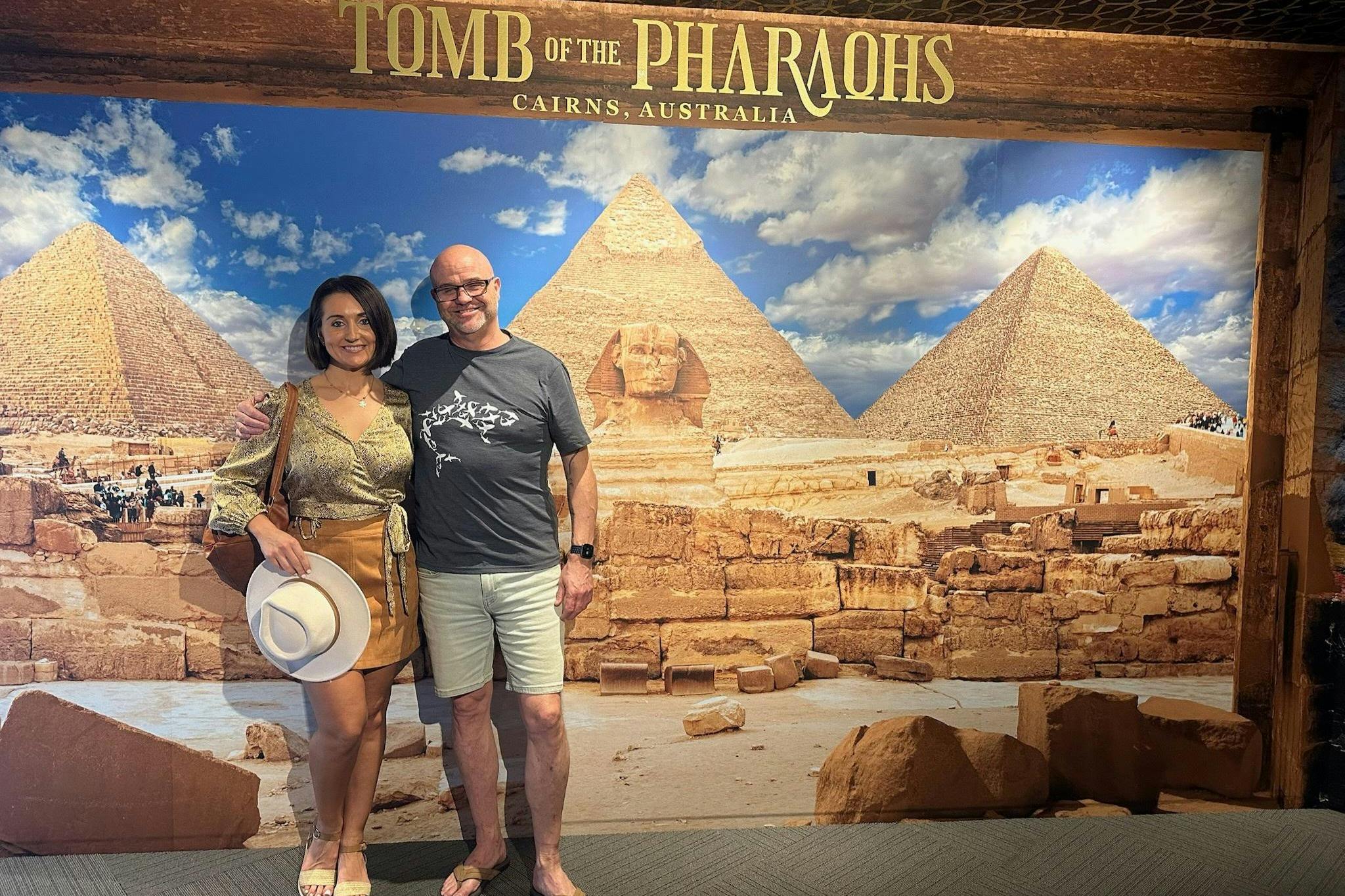 Dva lidé pózující před kulisou s pyramidami a Sfingou s textem „Hrobka faraonů, Cairns, Austrálie“.