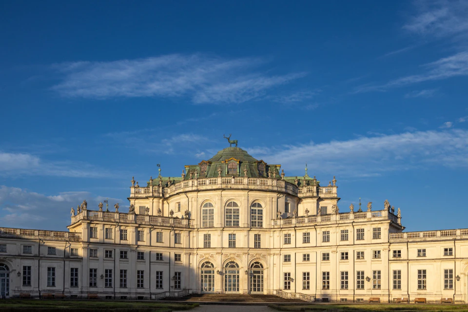 A historic palace with ornate architecture, a central dome, and symmetrical wings under a clear blue sky.