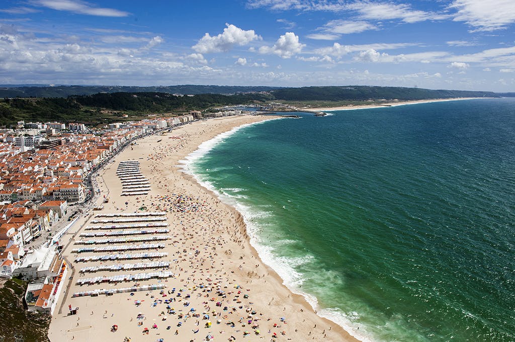 傘が並ぶ混雑したビーチ、日光浴、海水浴、建物や丘を背景にした鳥瞰図。