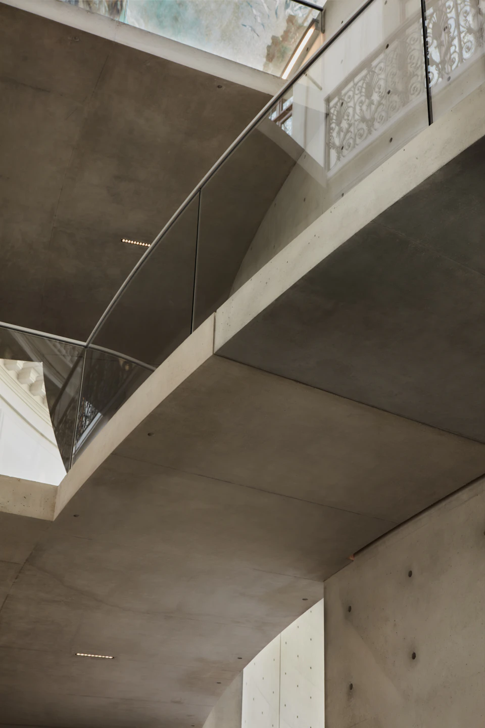 Modern interior with concrete walls and ceiling, glass railing, and metal supports viewed from below.
