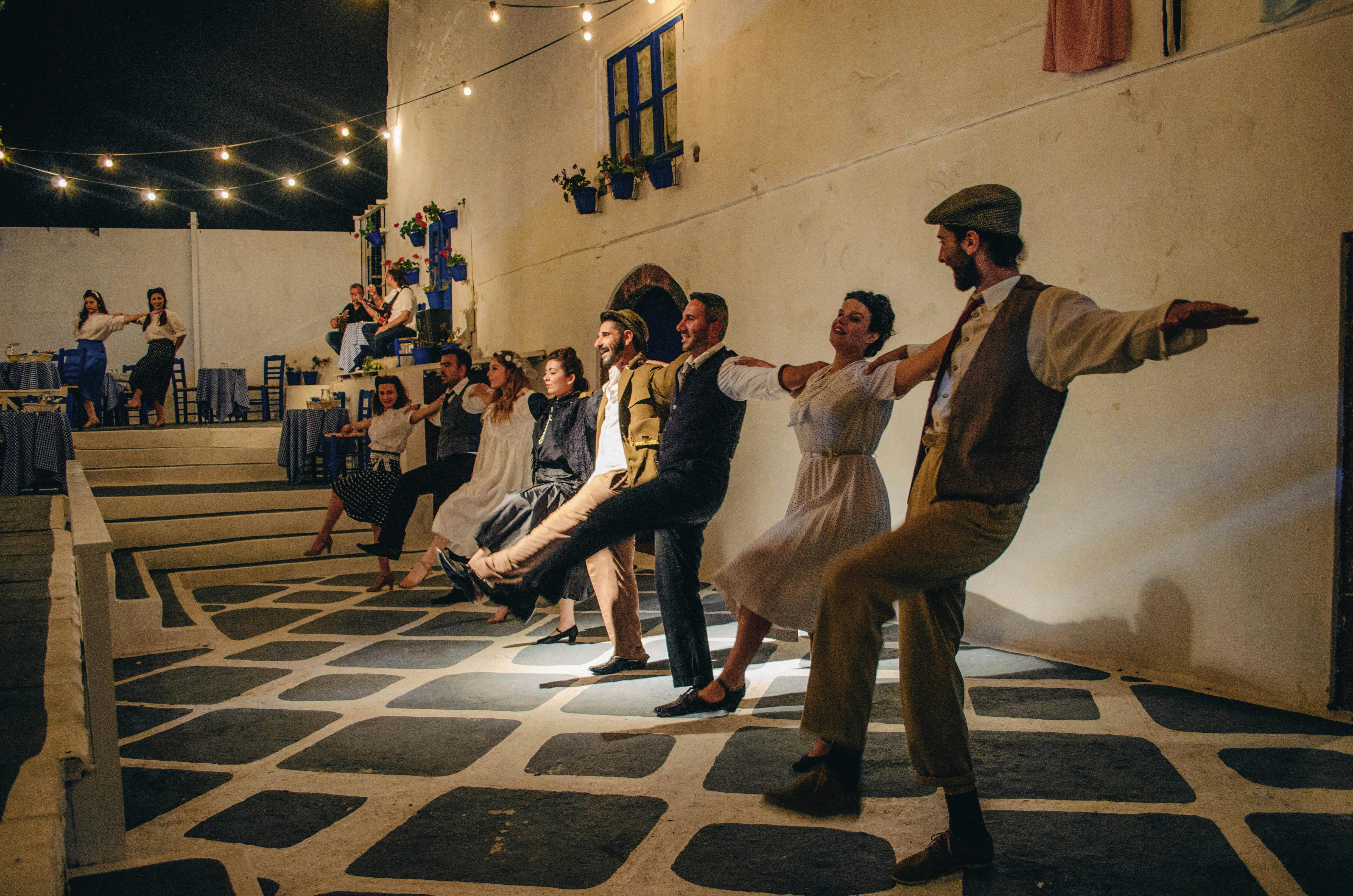 Un gruppo di persone che si esibisce in una danza tradizionale in un cortile con luci a corda ed edifici decorati di blu, di notte.
