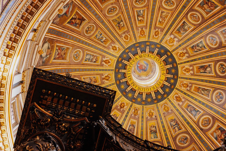 A close-up view of an ornate domed ceiling with intricate artwork and Latin text, highlighting its golden and detailed design.