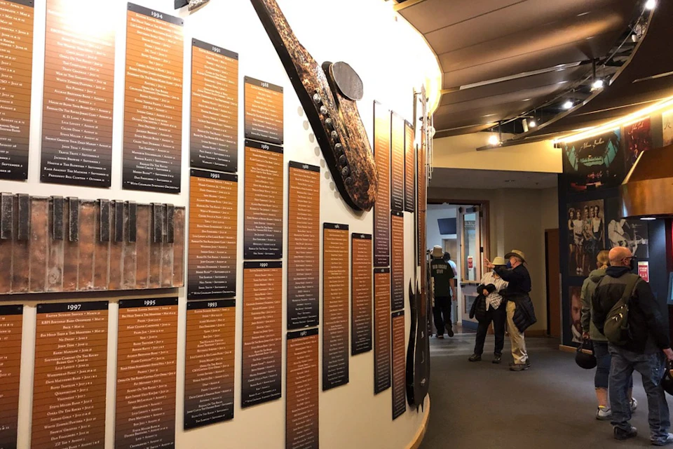 A museum exhibit features informational plaques on a curved wall and two visitors reading and taking photos.