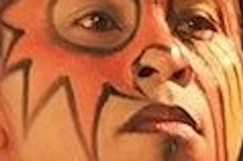 A person with face paint and traditional attire performs fire dancing at night, with a tribal mask in the background.