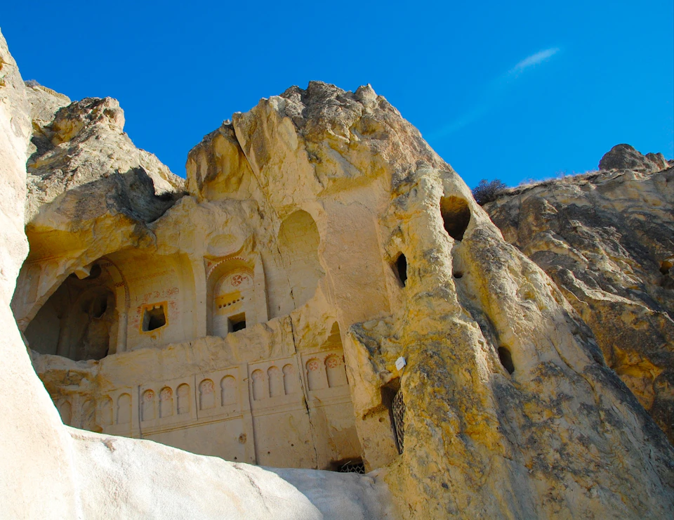 Ancient rock-cut architecture carved into a rocky cliff under a clear blue sky.