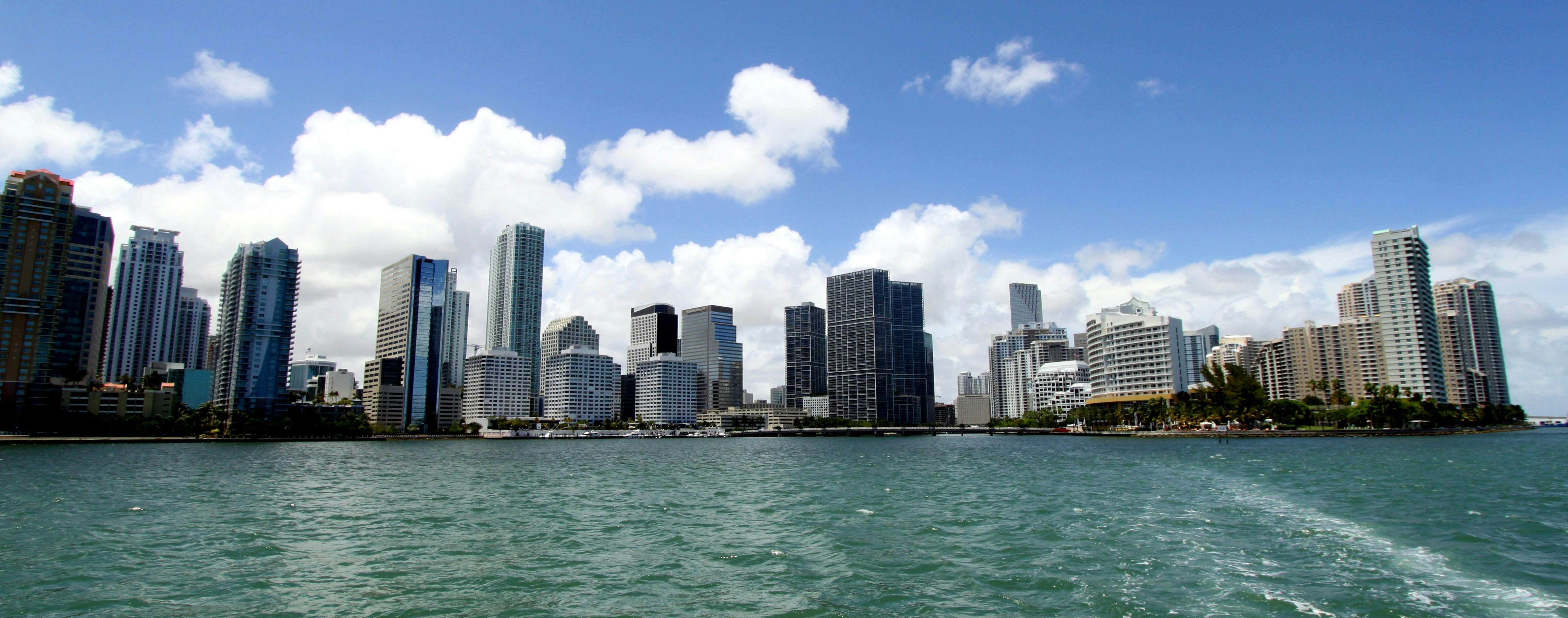 A city skyline with various high-rise buildings viewed across a body of water under a partly cloudy sky.