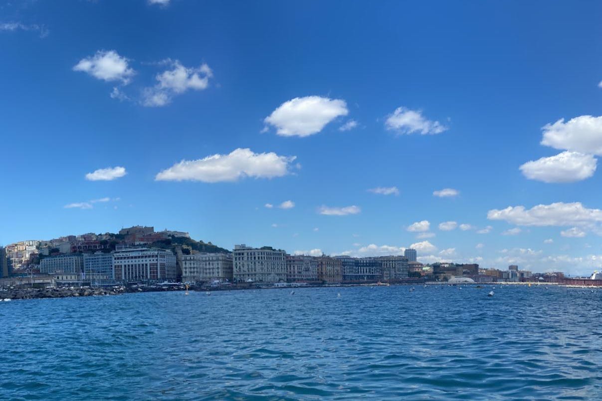 Un paisaje urbano frente al mar bajo un cielo azul claro con nubes dispersas, con edificios a lo largo de la costa y aguas tranquilas.