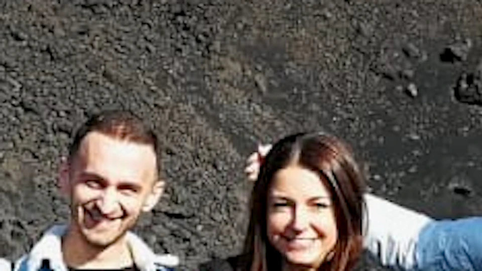 Five people standing in front of a rocky, volcanic landscape with a mountain and sparse snow patches in the background.