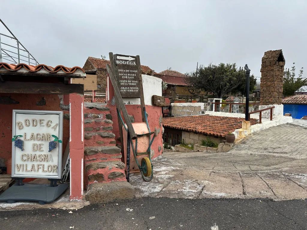 レンガの壁、古い手押し車、石段、ボデガの看板がある素朴なシーン。 背景にはタイル張りの屋根と曇り空。