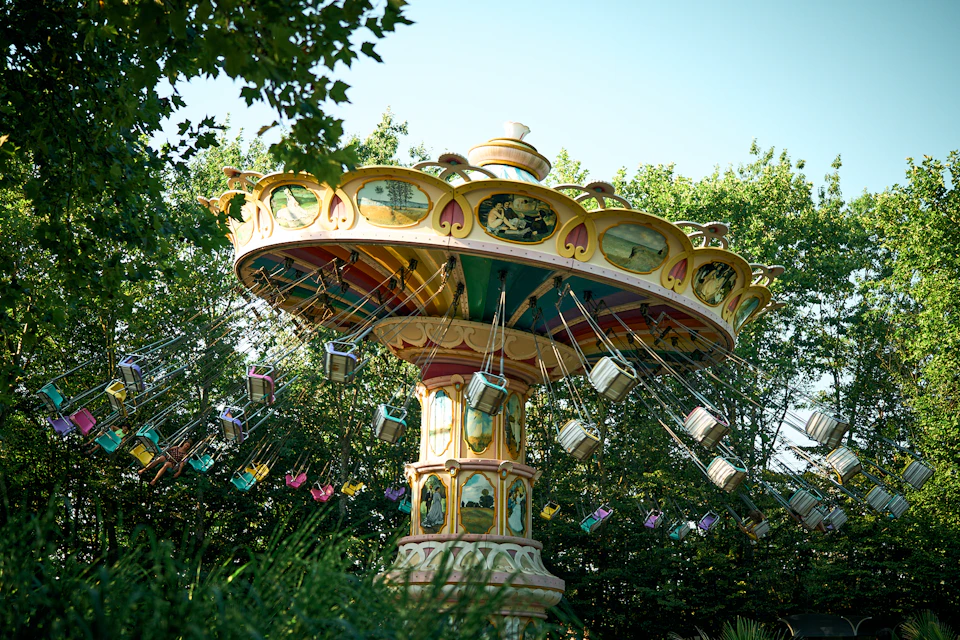 A colorful, vintage swing ride at an amusement park, with empty swings hanging, surrounded by trees and greenery.