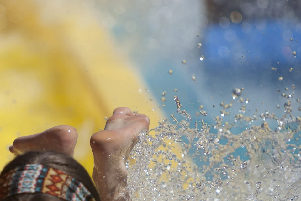 Two people on water slides holding blue mats, splashing through the water, with smiles on their faces.
