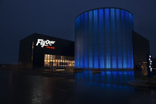 夜にアイスランドの建物の上に照らされたFlyOverは、その隣に青く照らされた円筒形の構造をしています。