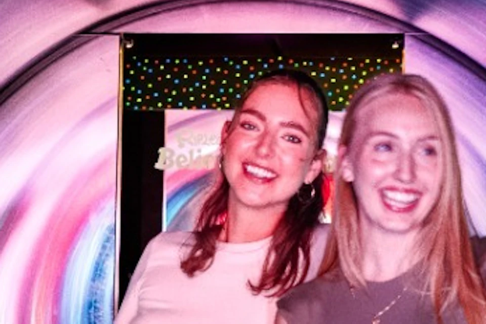 Four people stand on a railing in a tunnel with swirling colorful lights, smiling and posing for the camera.