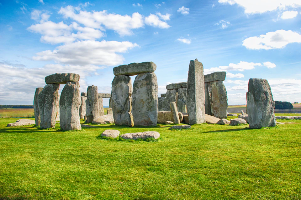 Stonehenge, a prehistoric monument, featuring large standing stones on a grassy field under a partly cloudy sky.