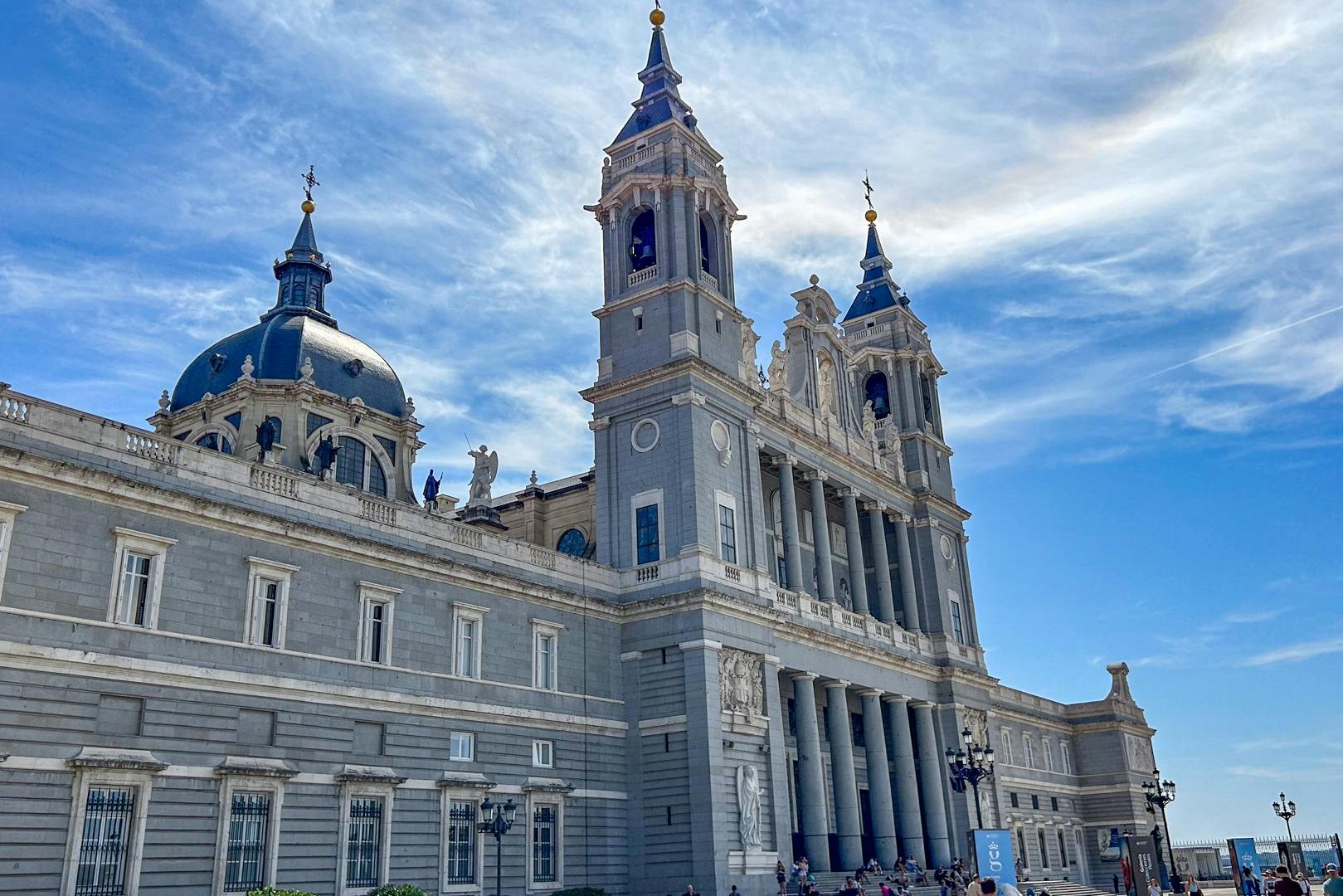 Um grande edifício com grandes colunas, torres ornamentadas e uma cúpula sob um céu azul brilhante com algumas nuvens.