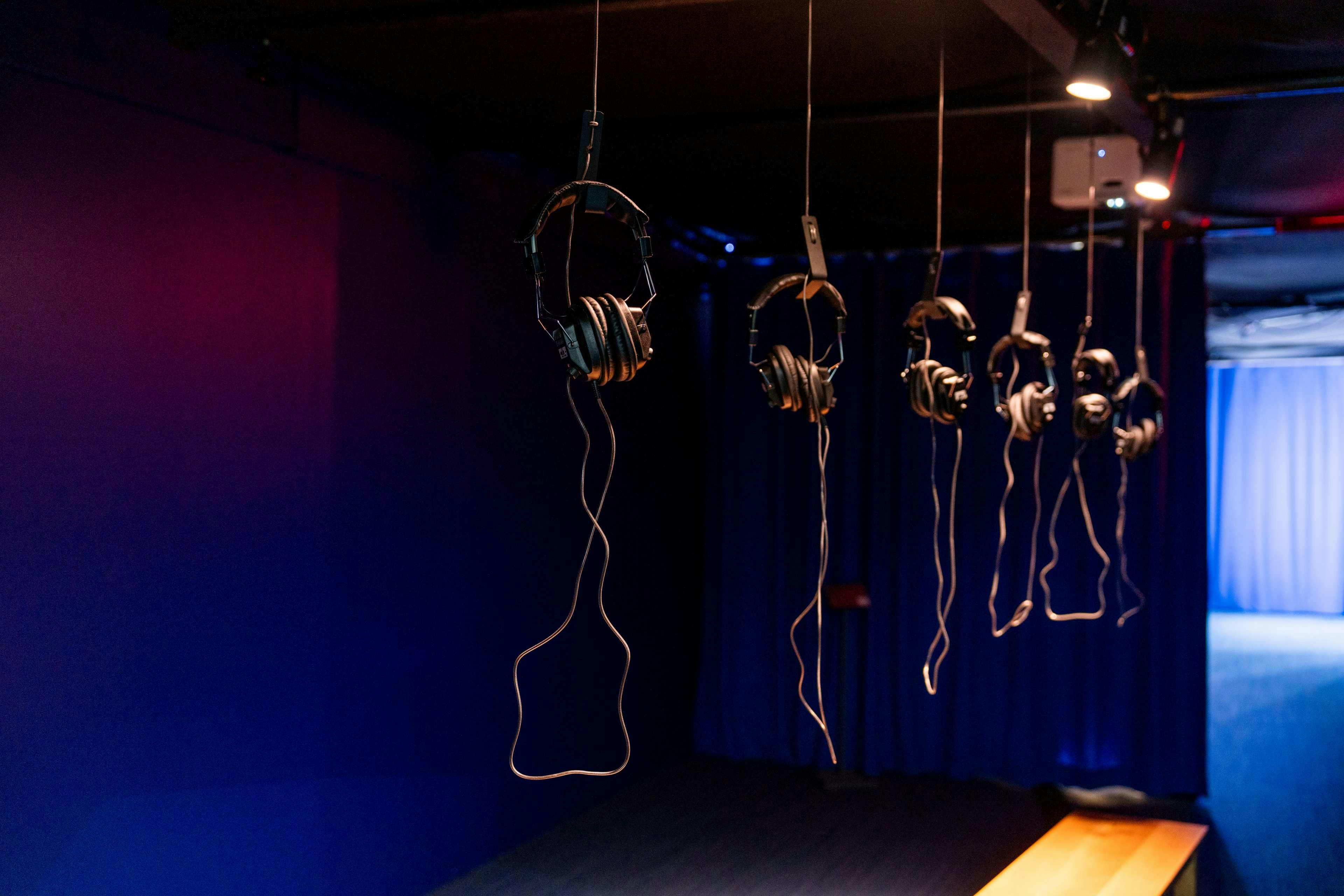 Several headphones hang from the ceiling in a dimly lit room with dark blue walls and minimal lighting.