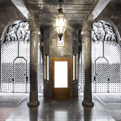 Utsmyckad entré med marmorpelare, en trädörr, välvda fönster, smidesjärnsportar och en dekorativ lykta.