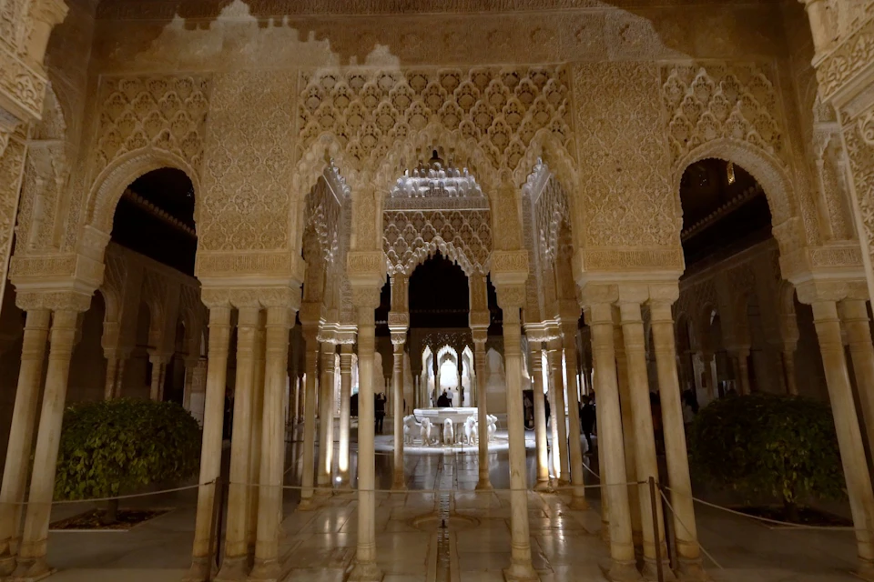 Intricately carved stone columns and arches in a dimly lit historic courtyard with a central decorative fountain.