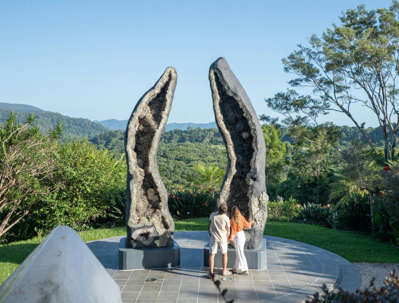 緑と晴れた空に囲まれた屋外の大きなジオード彫刻の前に2人の人物が立っています。