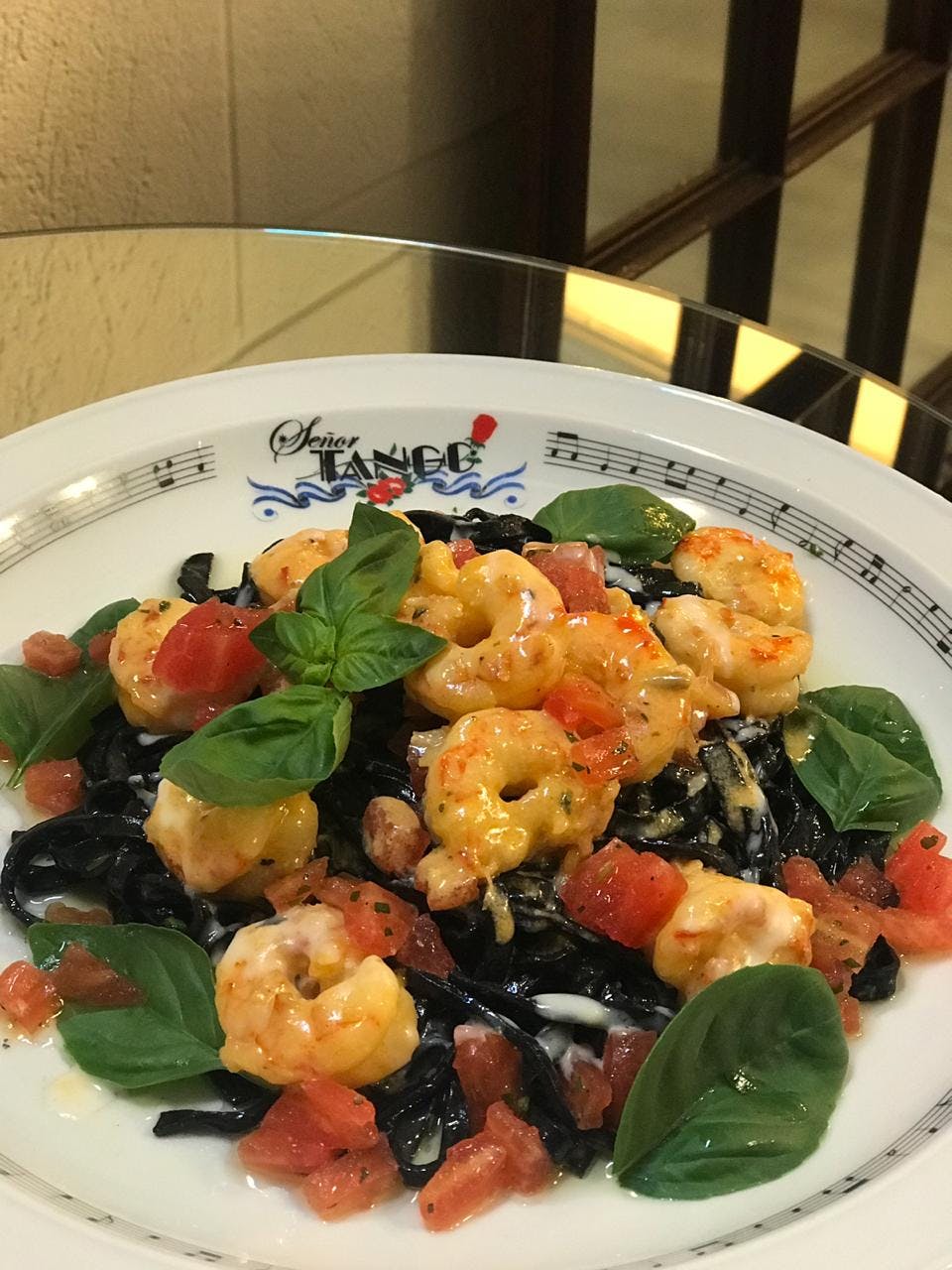 Plate of shrimp and pasta garnished with basil and diced tomatoes on a decorated restaurant plate with musical notes.