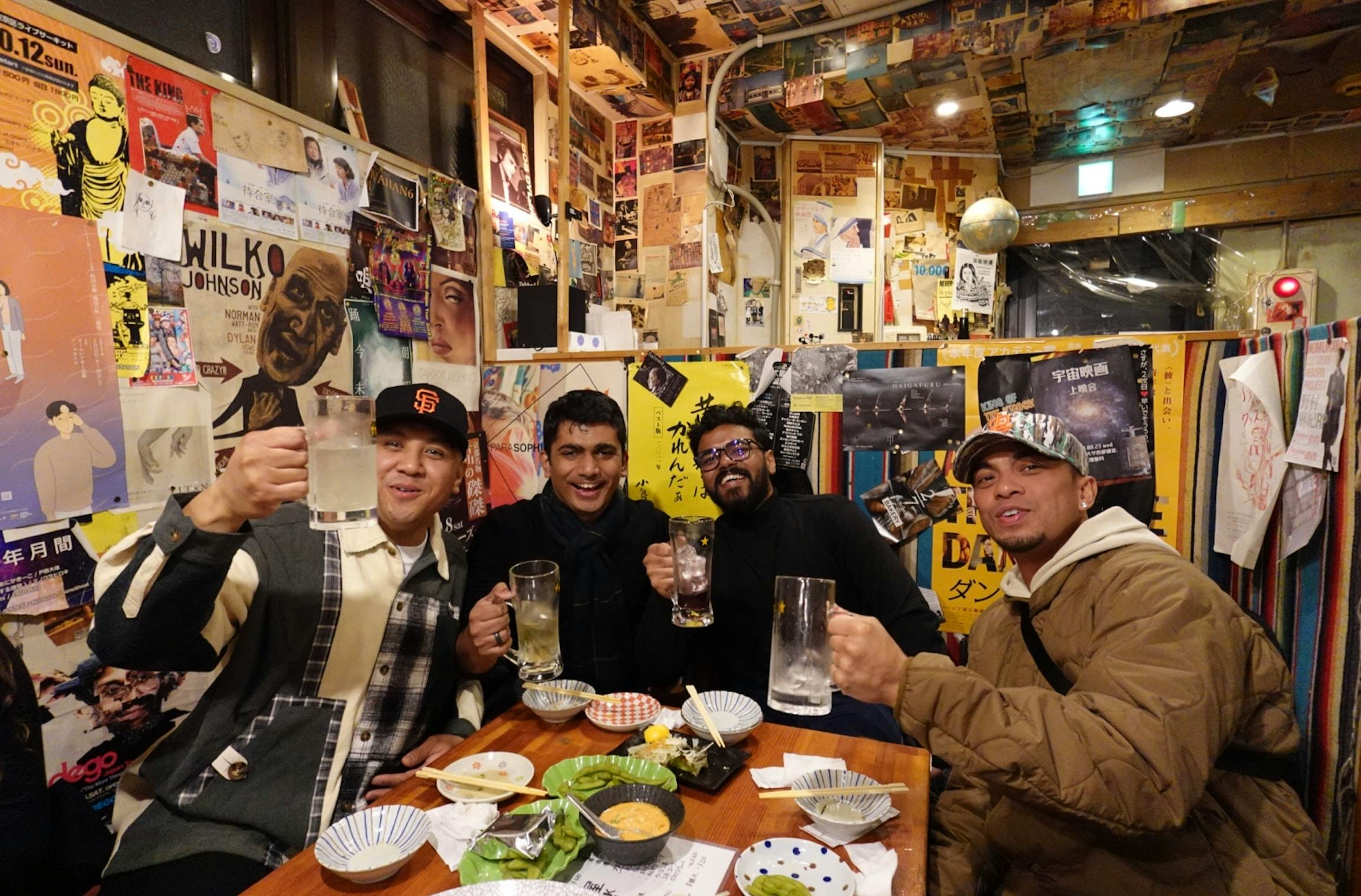 Three friends enjoying drinks and food at a cozy restaurant with eclectic decor and posters on the walls.