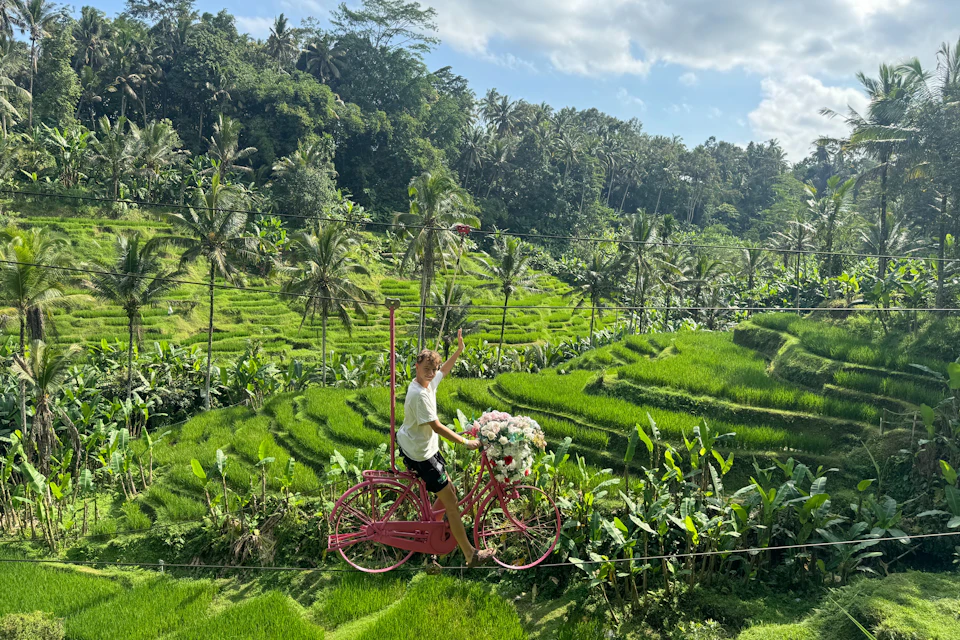 A guy waving and smiling to the camera while cycling on a Skybike over the rice terraces of U Fun Field park