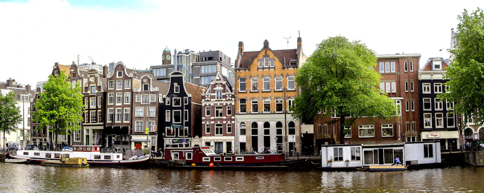 A canal in front of traditional Dutch buildings with gabled facades and a red houseboat docked along the water.