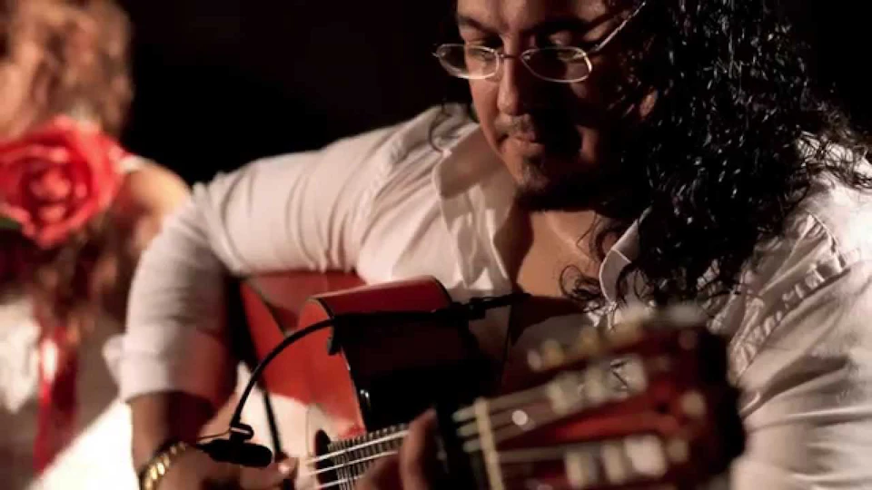 A person in glasses and a white shirt playing an acoustic guitar.