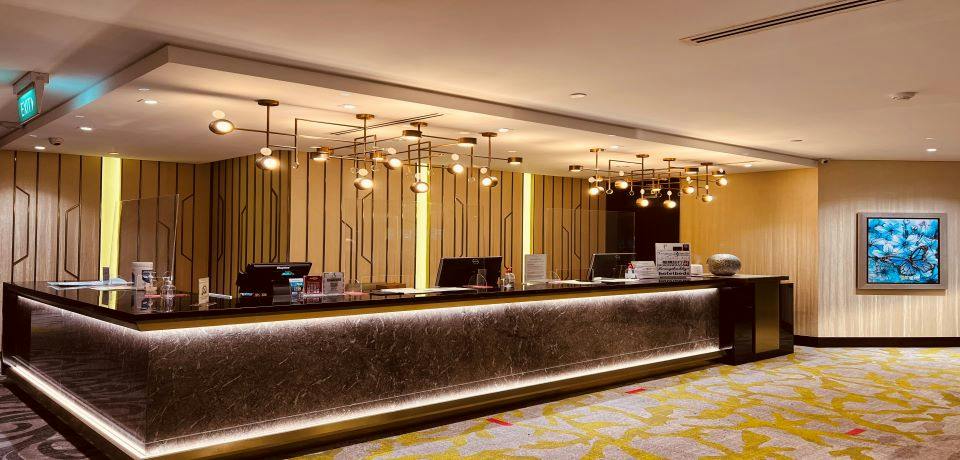 A modern hotel reception desk with decorative lighting, polished counters, and a patterned carpeted floor.