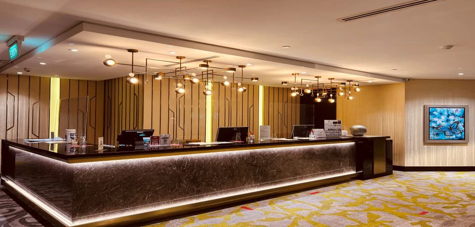 A modern hotel reception desk with decorative lighting, a marble counter, and a patterned carpeted floor.