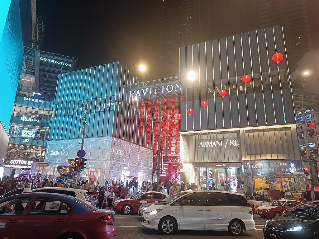 ディオール、無印良品、アルマーニなどのライトアップされたショップが軒を連ねる夜の都会のショッピングエリア。 前景には赤いランタンと車。