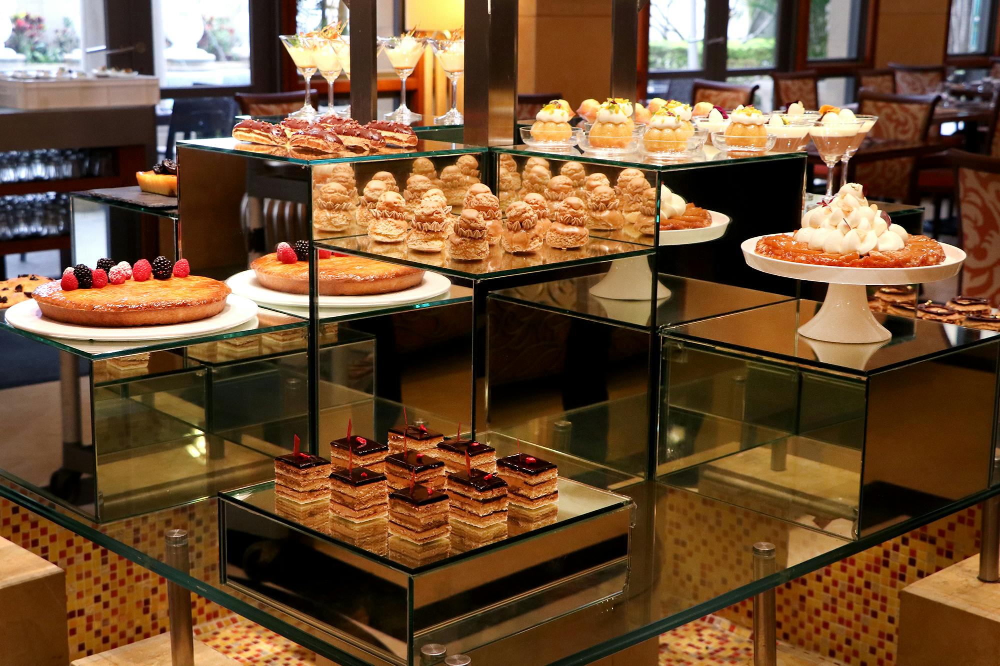 An elegant dessert buffet display with various pastries and cakes arranged on glass shelves in a restaurant setting.