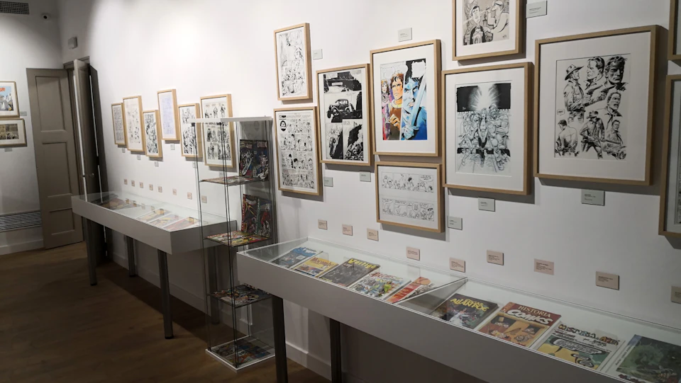 Gallery with framed comic art on the walls and display cases holding comic books. A glass cabinet holds additional comic items.