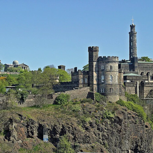 Stentorn, monument och historiska byggnader sitter på en stenig, grön kulle under en klarblå himmel.