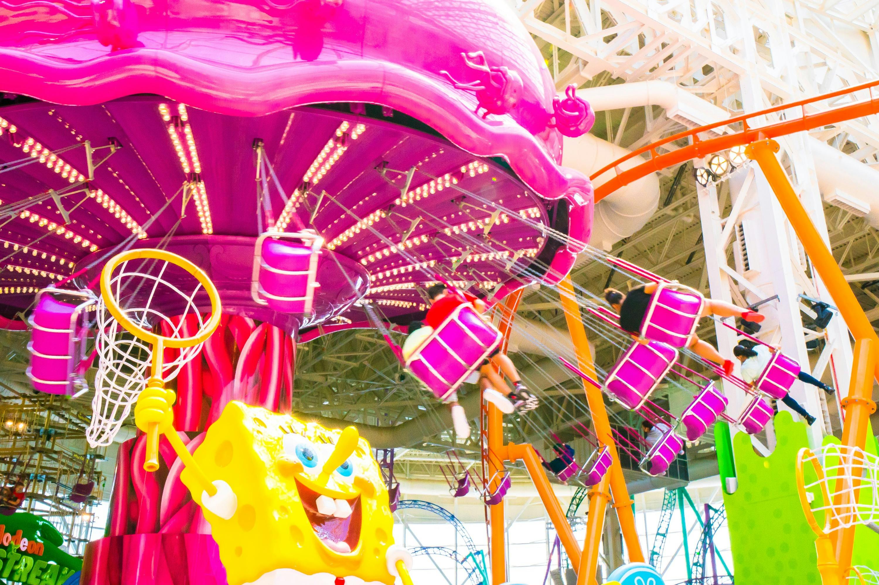 A vibrant pink amusement park ride with spinning seats, SpongeBob character decor, and people enjoying the ride.