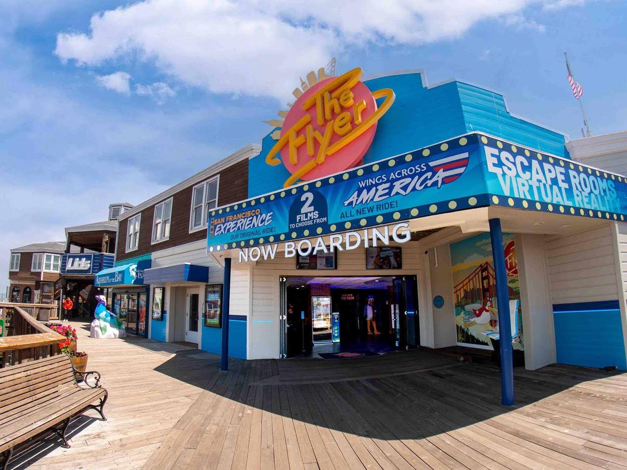 Вход для аттракционов на открытом воздухе на променаде с большим значком «The Flyer» и баннером «Now Boarding».