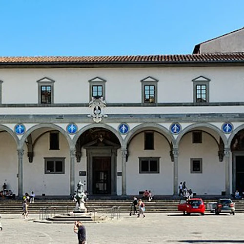 En stor byggnad med valv och fönster, med statyer, en ryttarskulptur och människor som går på gården.