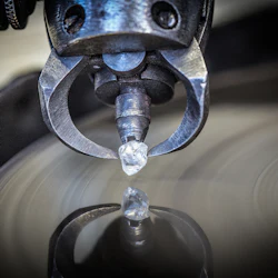 Närbild av en oslipad diamant som hålls av en metallklämma som reflekteras på en yta.