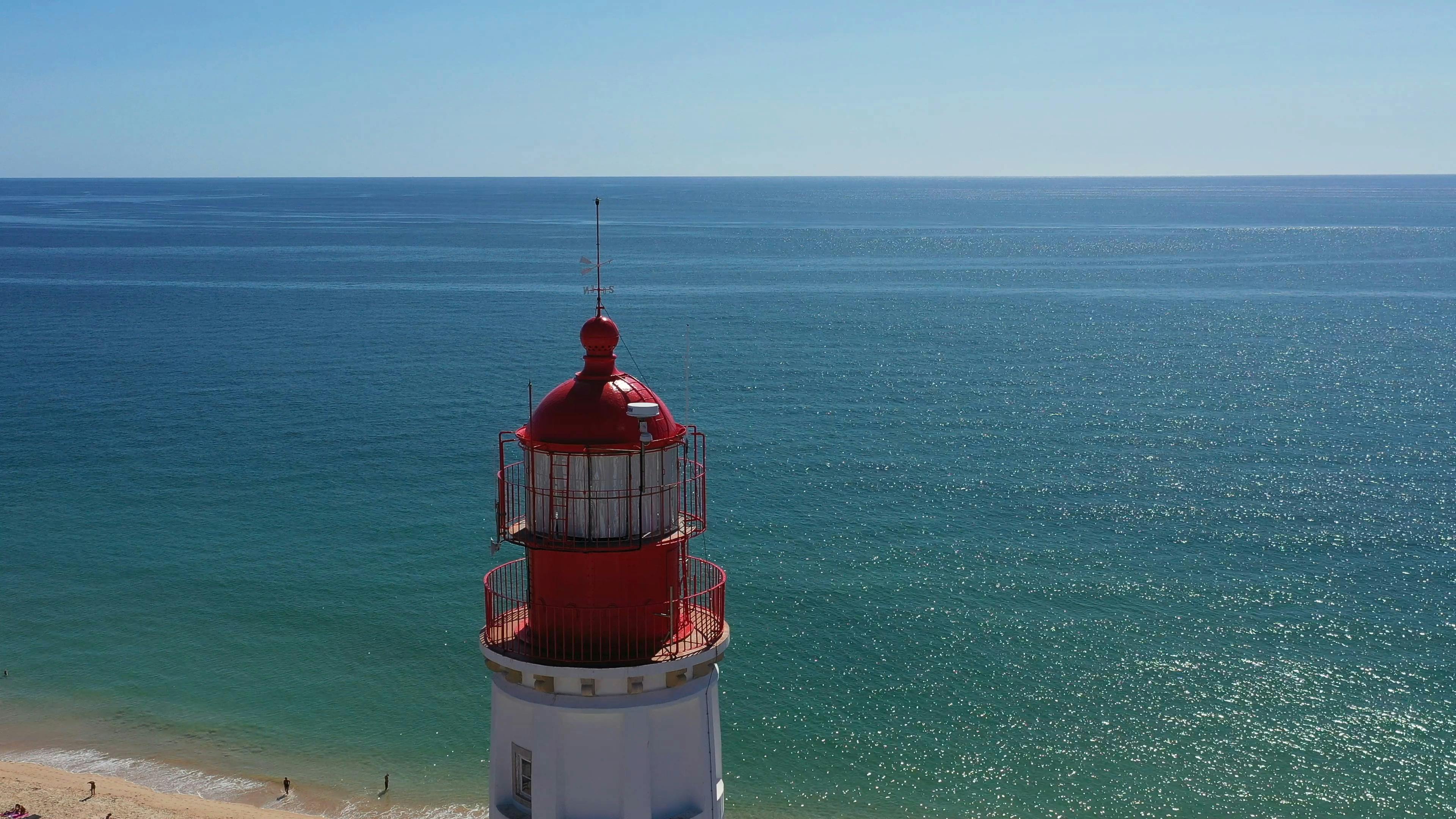 Κόκκινος και λευκός φάρος με θέα έναν ήρεμο, απέραντο ωκεανό κάτω από έναν καταγάλανο ουρανό. Αμμώδης παραλία ορατή στη βάση.